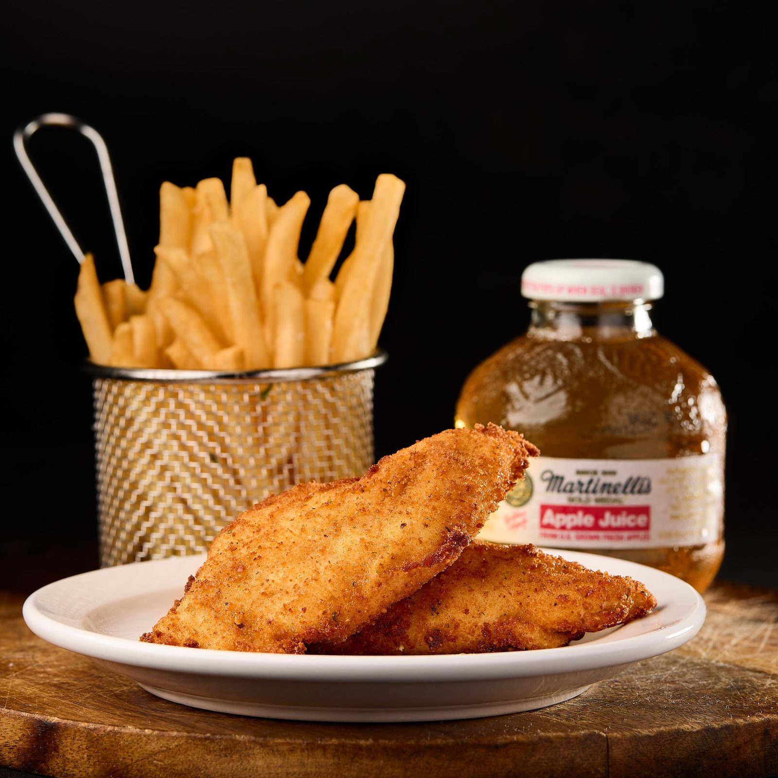 Plate of crispy chicken tenders with fries and a bottled apple juice