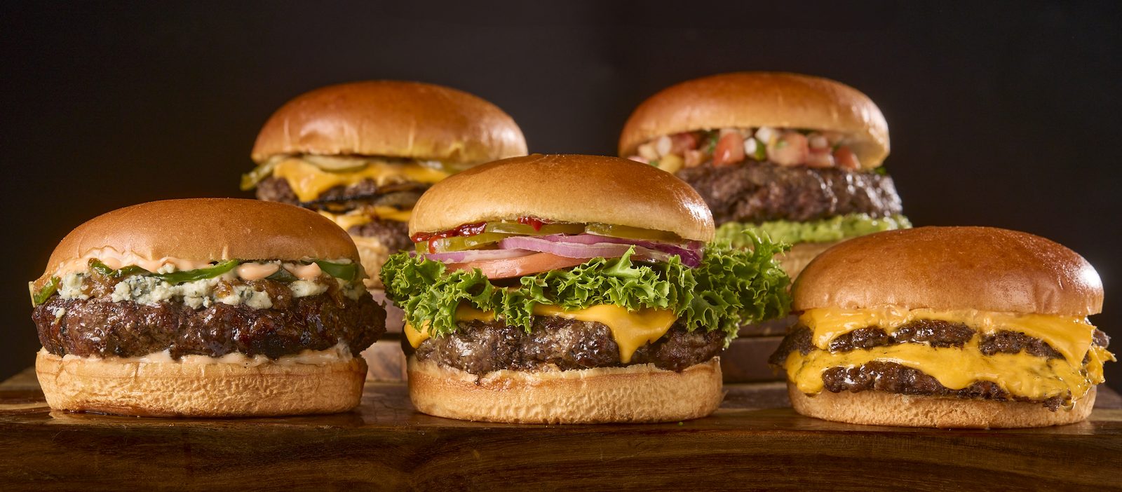 A spread of five different 3:33 Burgers on a dark table